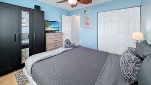 Quarto com cama, ventoinha no teto, televisão e guarda-roupa.