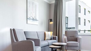 Ein modernes Wohnzimmer mit einem grauen Sofa, einem grauen Sessel, einem kleinen runden Tisch und einer Stehlampe.