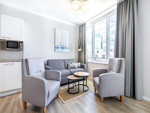 A modern living room with a grey sofa, two armchairs, a small coffee table, and a kitchen area with a microwave. - 4 Star Holiday Home in Travemunde (Lübeck)