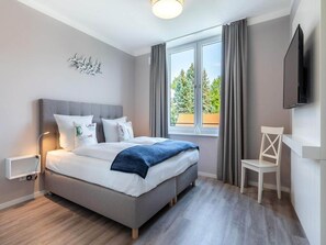 A bedroom with a bed, a desk, a chair, a TV, and a window with curtains. - 4 Star Holiday Home in Travemunde (Lübeck)