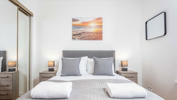 Ein ordentlich gemachtes Bett mit Kissen, Nachttischlampen, einem Wandbild und einem Spiegel.