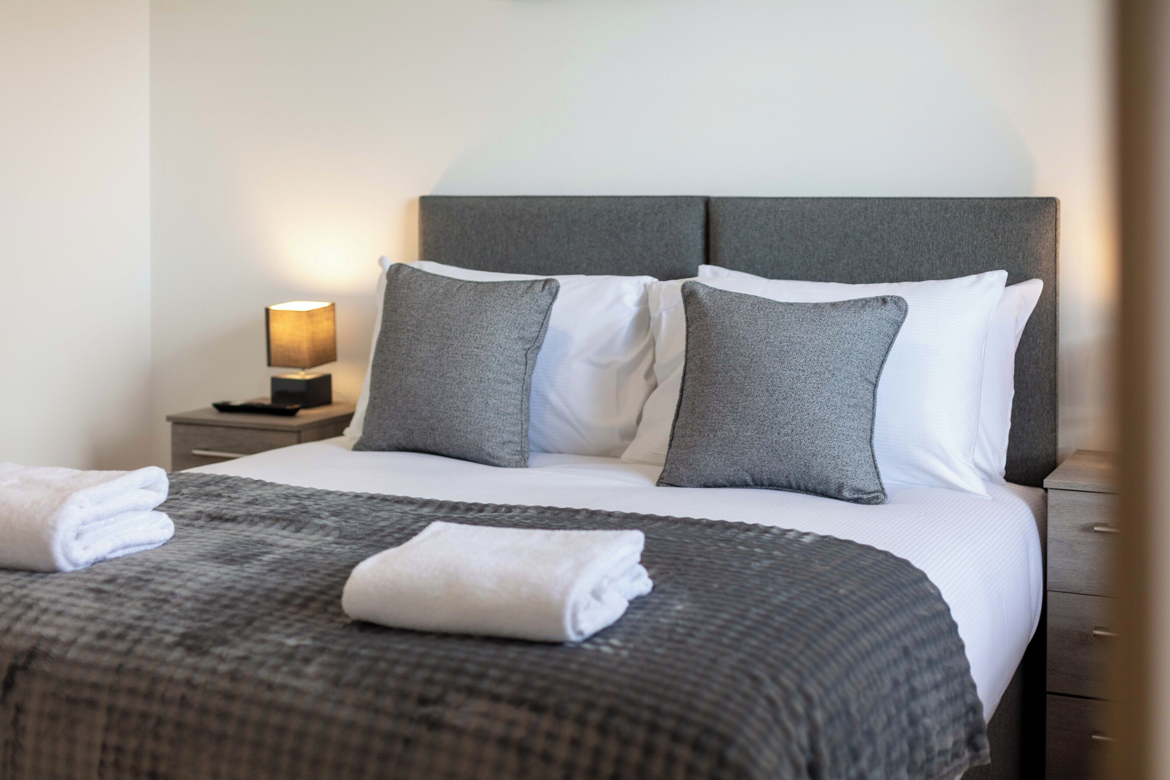 A neatly made bed with a grey headboard, white pillows, and a grey blanket.
