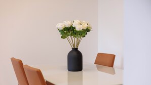 Ein Tisch mit einer Vase voller weißer Blumen, zwei braune Stühle und einer weißen Tischplatte.