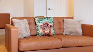 Ein braunes Ledersofa mit zwei Kissen, eines mit Blumenmuster und eines schlicht.