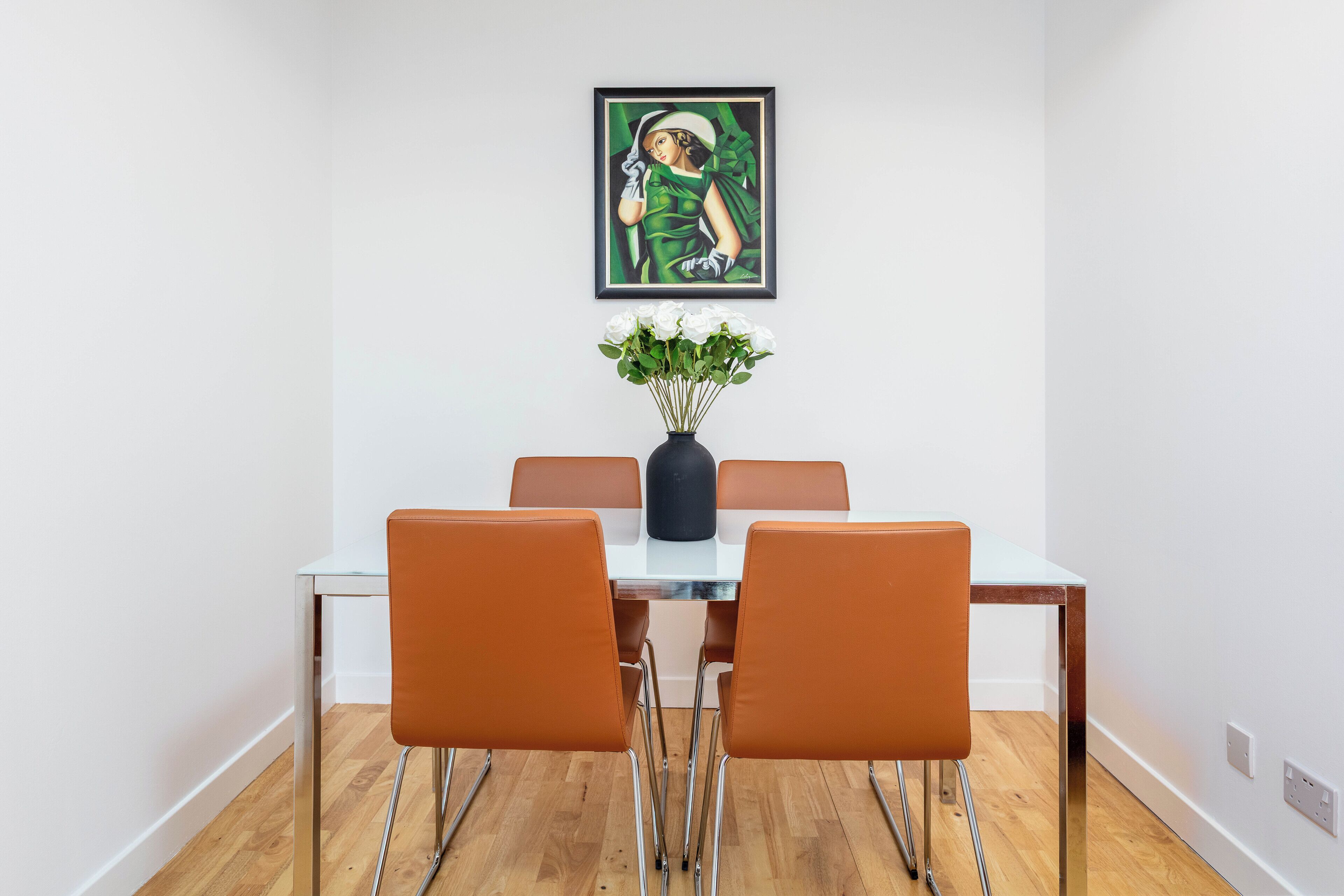 Un comedor con una mesa, sillas, un jarrón con flores y un cuadro en la pared.