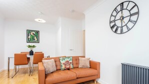 Ein Wohnzimmer mit einer Couch, Sesseln, einem Tisch, einer Uhr und einer Heizung.