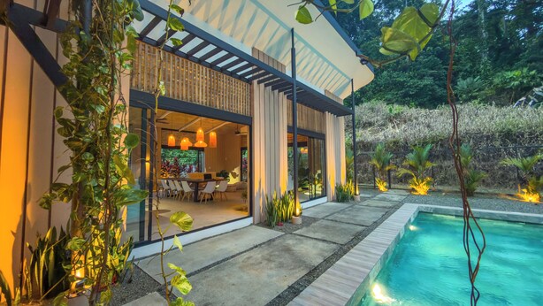 Ein modernes Haus mit Swimmingpool, Essbereich im Freien und üppiger Bepflanzung.