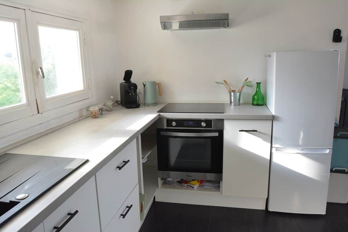 A compact kitchen with a stove, oven, and refrigerator, white cabinetry, and a window providing natural light.