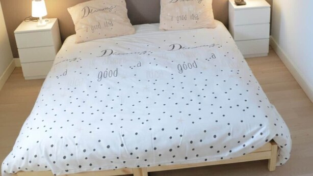 Un lit recouvert d’une couvre-lit à pois blancs, deux tables de chevet avec des lampes et des coussins ornés de motifs textuels.