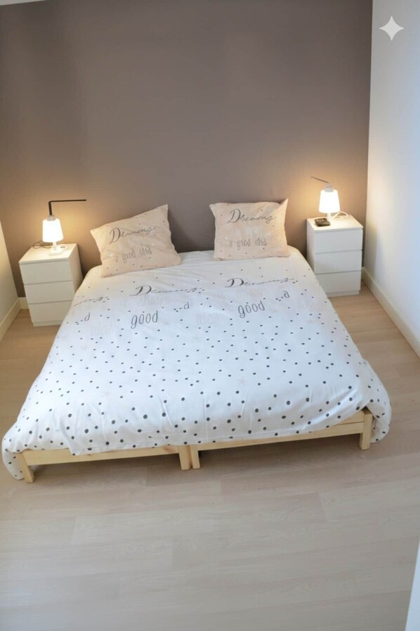 Een bed met een wit stippenbed overtrek, twee nachtkastjes met lampen, en kussens met tekst.