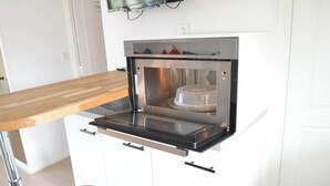 Une cuisine compacte dotée d’un four encastré, d’un plan de travail en bois et de meubles de rangement blancs.