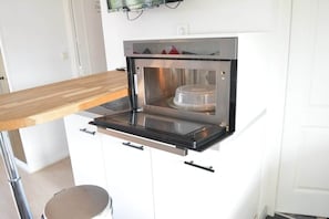 Une cuisine compacte dotée d’un four encastré, d’un plan de travail en bois et de meubles de rangement blancs.