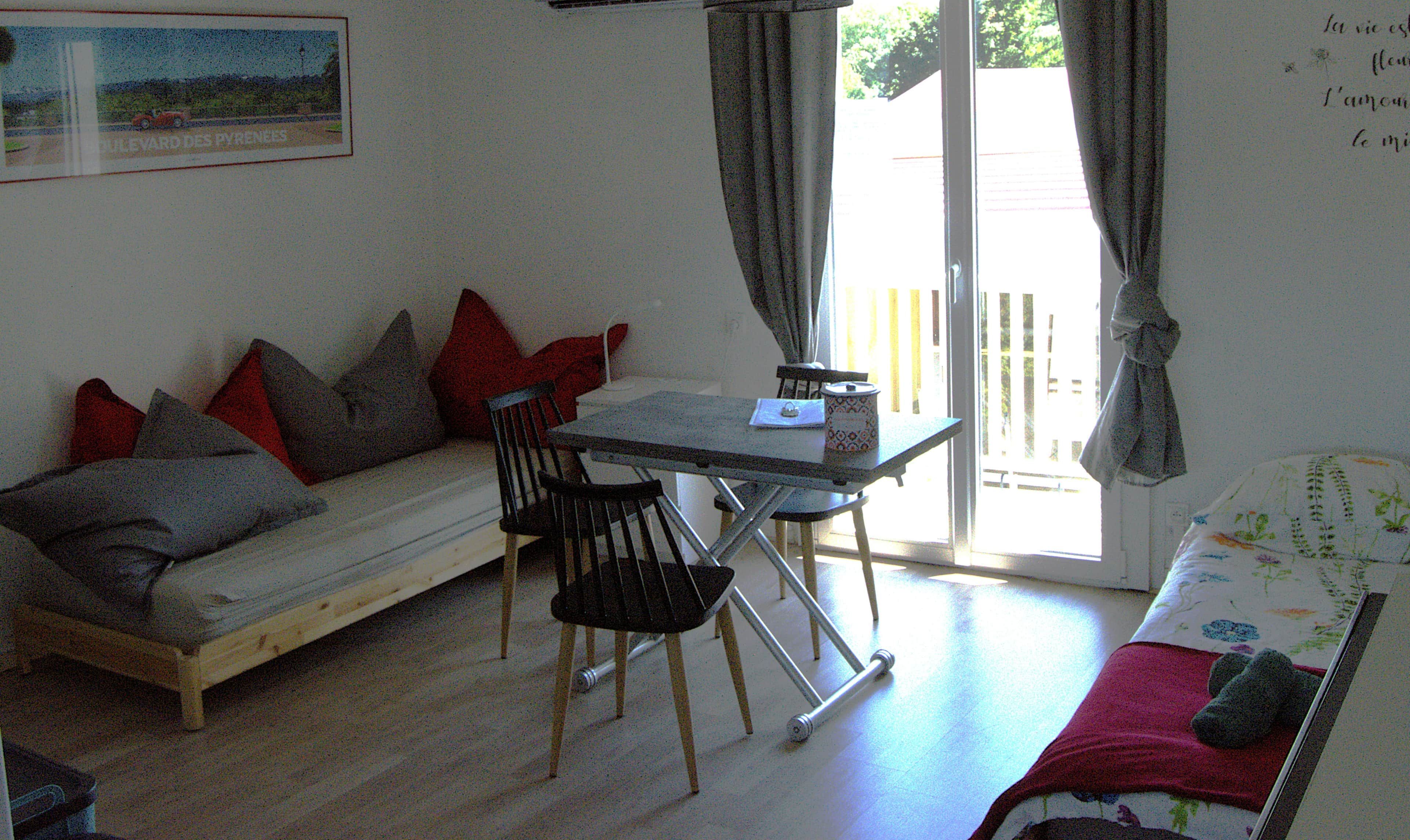 A small, cozy room with a sofa, a dining table with chairs, and a window with curtains.
