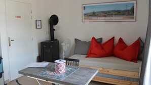 Une pièce avec un canapé, une table sur laquelle se trouve un rouleau de papier, un radiateur noir, un ventilateur et un tableau encadré accroché au mur.