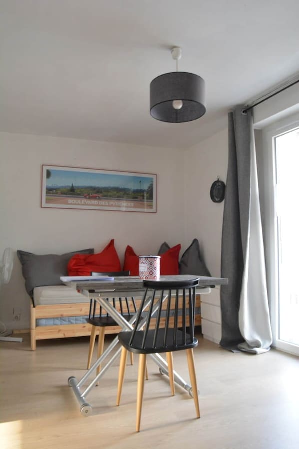 Un salon moderne comprenant une table à manger, des chaises, un canapé, un tableau et une grande fenêtre avec des rideaux.