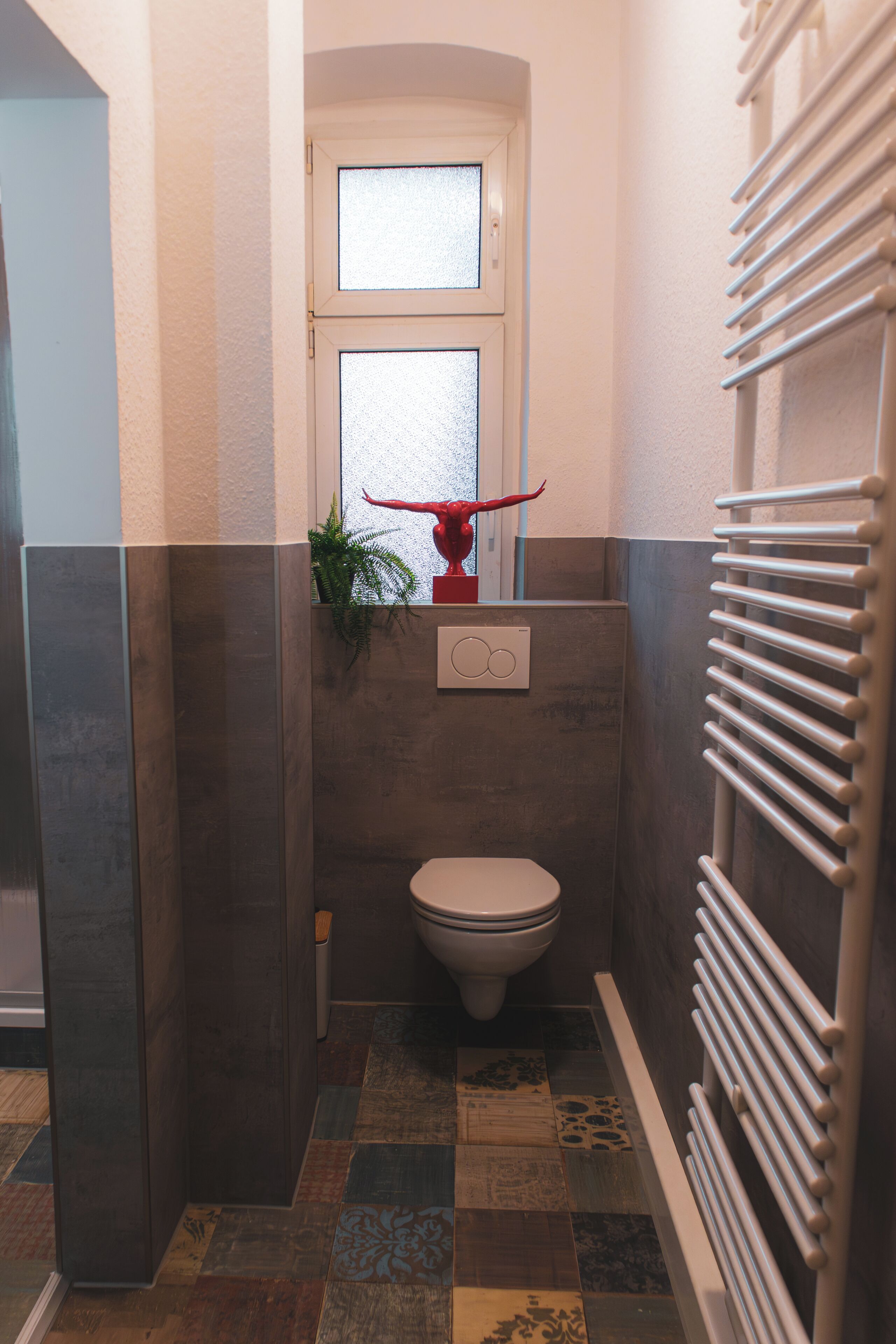 A bathroom with a toilet, a window, a radiator, and a plant.