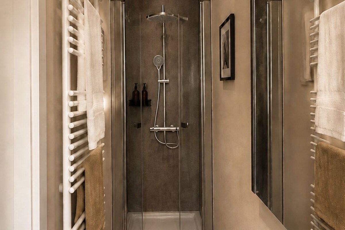 Un baño moderno con ducha envuelta en vidrio, un lavamanos blanco y un perchero para toallas.