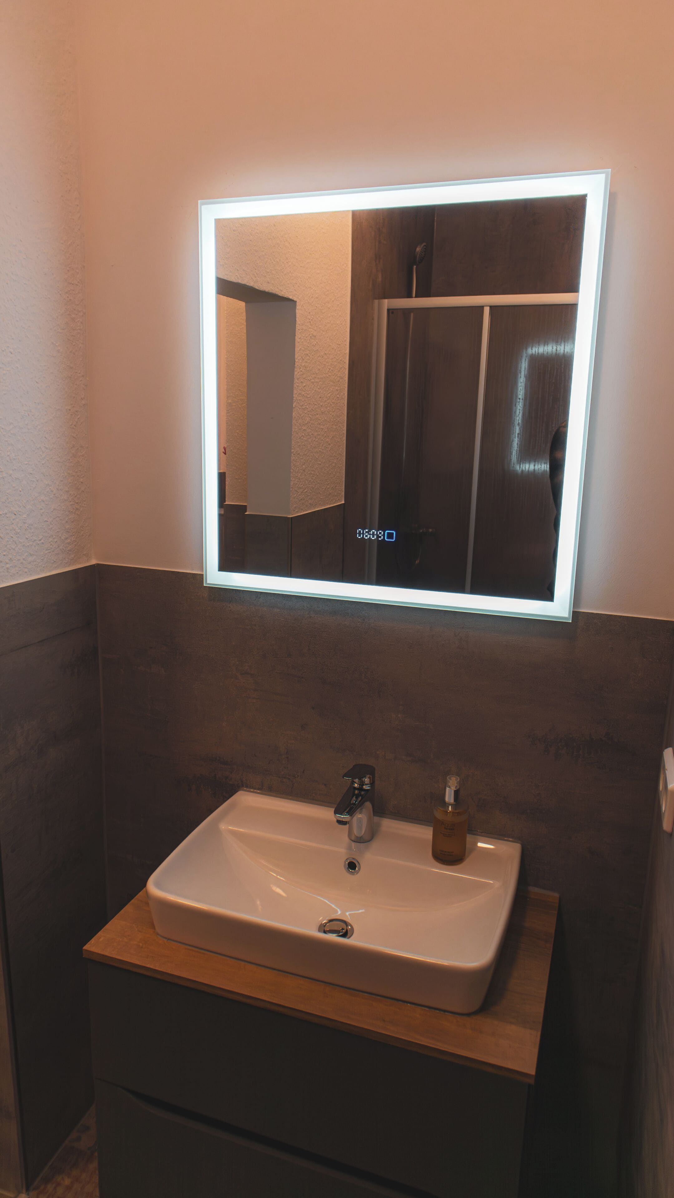 A bathroom with a rectangular sink, a mirror with a light, and a dark wall.