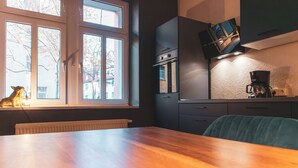 A kitchen with a wooden table, a TV mounted on the wall, and a window with a view of buildings outside. - Cityloft Erfurt (Erfurt)