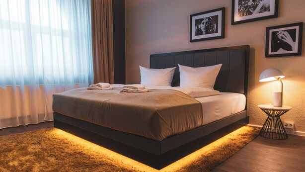 A neatly made bed with pillows and a blanket, a bedside lamp, and a rug. - Cityloft Erfurt (Erfurt)