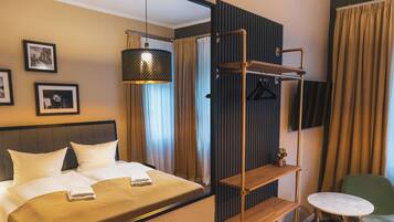 A hotel room with a bed, a hanging light fixture, a TV mounted on the wall, and a small table with a chair.