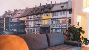 A room with a sofa, a potted plant, and a wall mural of European-style buildings. - Cityloft Erfurt (Erfurt)