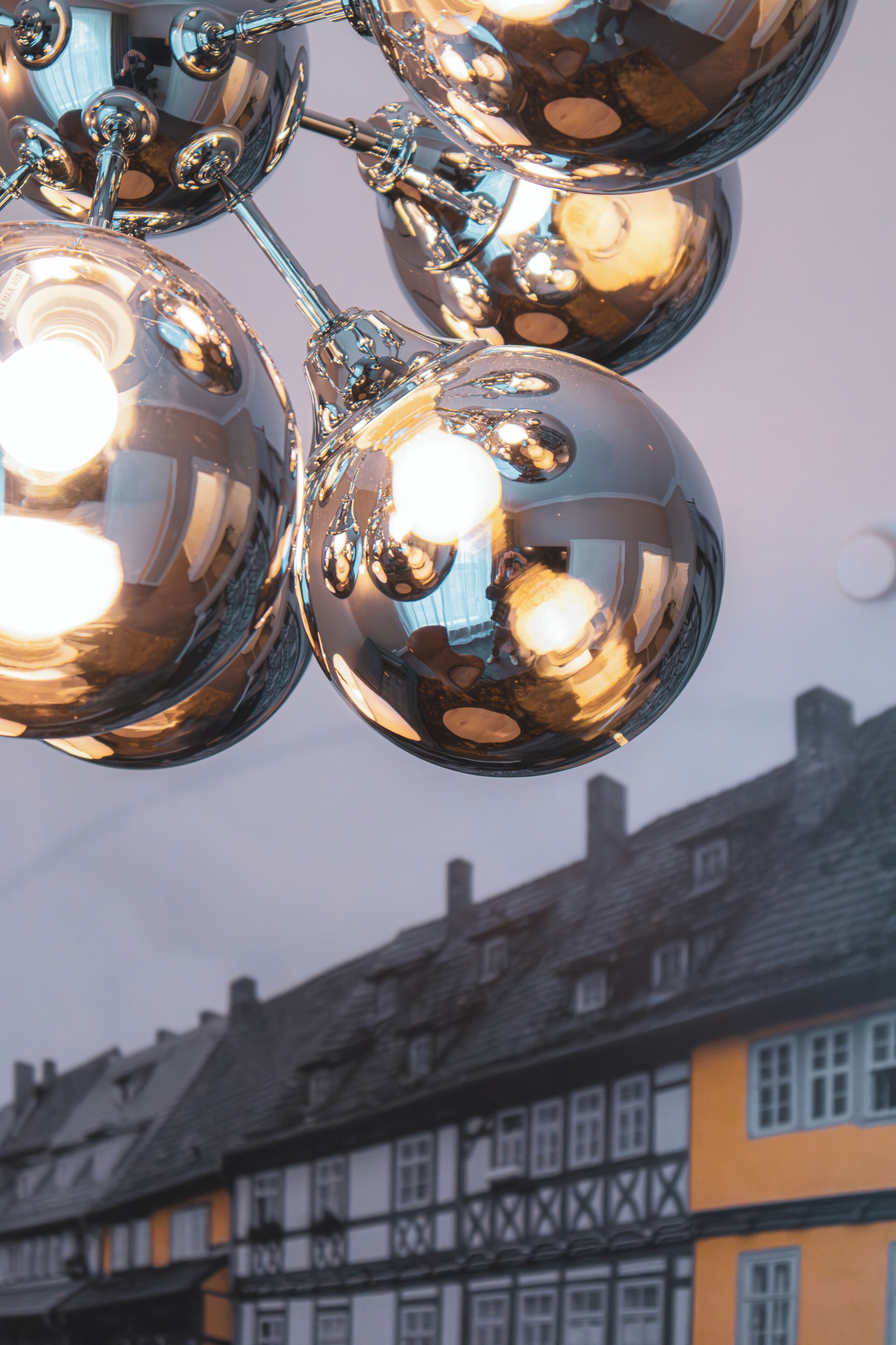 A close-up of shiny metallic spherical objects, likely part of a decorative installation, with a blurred background featuring traditional half-timbered buildings.
