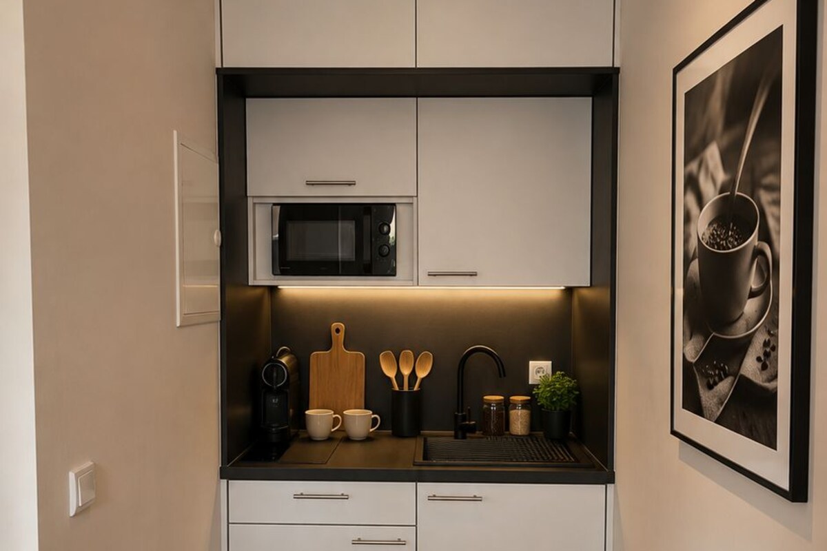 Una cocina compacta con armarios blancos, un microondas, una cafetera y un cuadro en la pared.