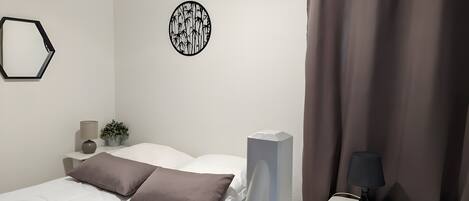 A bedroom with a bed, pillows, a bedside table with a lamp, a wall decoration, and a curtain.