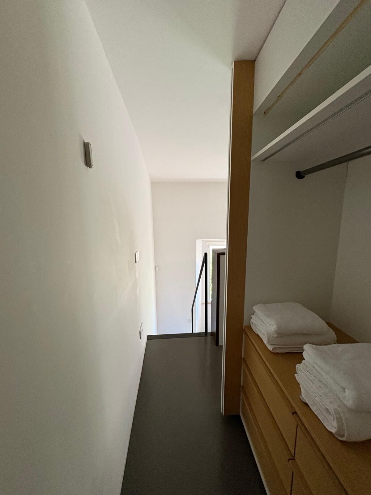 A narrow hallway with a wooden bench and a stack of white towels on the right.