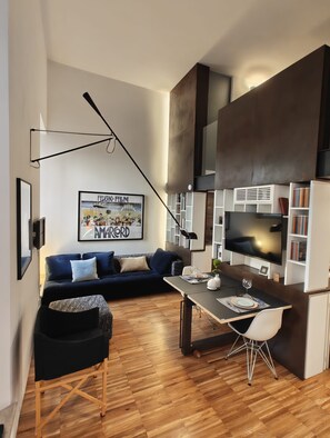 Una sala de estar moderna con un sofá azul oscuro, una mesa de comedor con sillas, un televisor y estanterías.