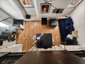 Un interior moderno con piso de madera, un sofá azul, una escalera y un tragaluz.