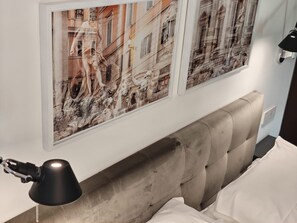 Un dormitorio con cabecera, cama, mesita de noche, lámpara y dos cuadros en la pared.