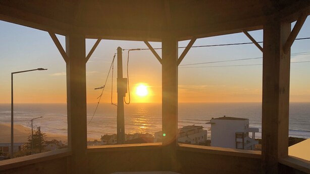 A wooden deck with a view of the sunset over the ocean, a streetlight, and a utility pole.