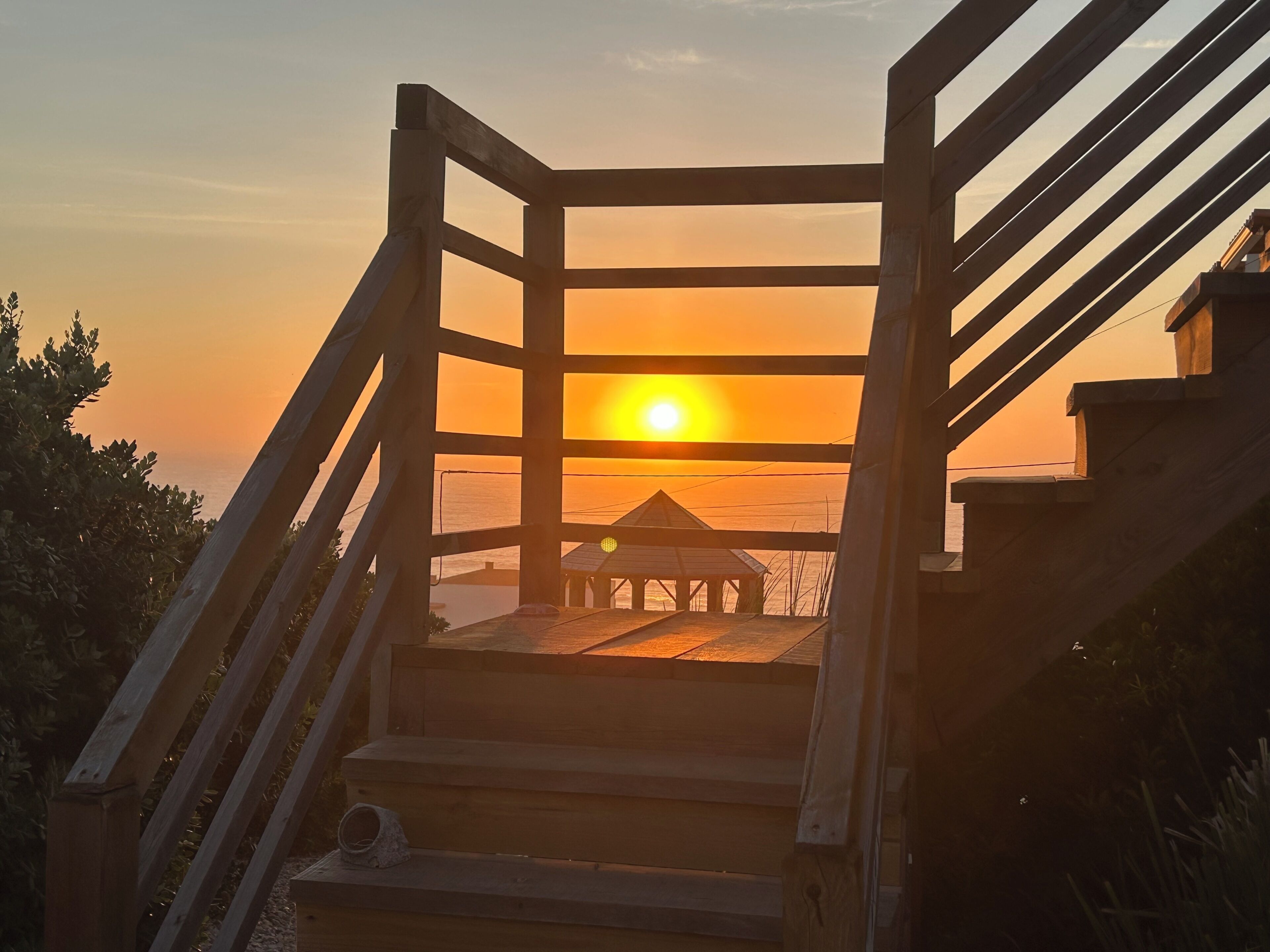 Una escalera de madera lleva a una terraza de madera con vistas al atardecer sobre el agua.