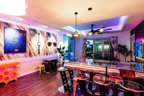 Un área de bar moderna con una mesa de vidrio, taburetes y un ventilador de techo.