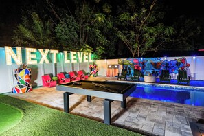 Zona de piscina al aire libre con mesa de billar, sillones de descanso y un cartel que dice 'NEXT LEVEL'.