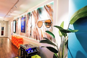 Une pièce avec un mur décoré d’un motif imitant le marbre, un présentoir pour passeports, des lunettes de soleil, une plante et une console de jeux.