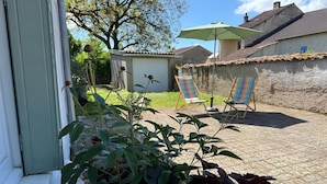 Eine Terrassenfläche mit Topfpflanzen, Gartenmöbeln und einem Gebäude im Hintergrund.
