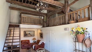 Ein rustikaler Innenraum mit Schlafgalerie, Holzbalken, einem Essbereich und einer Treppe.