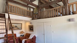 Ein Loft-Zimmer mit freiliegenden Holzbalken, einem braunen Ledersofa, einer Treppe, einer weißen Tür und einem Bild an der Wand.