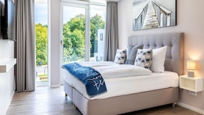A modern bedroom with a large bed, a television, a painting, and a view of greenery outside. - 4 Star Holiday Home in Travemunde (Lübeck)