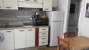 Eine kompakte Küche mit weißen Schränken, einer Mikrowelle, einem Kühlschrank, einer Spüle und einem Esstisch mit Stühlen.