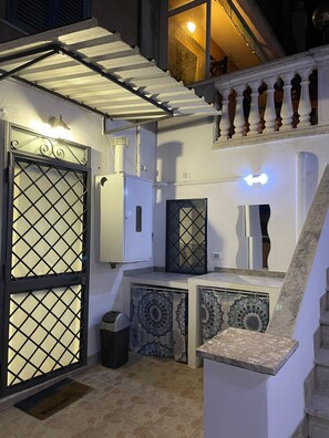 Un espacio al aire libre cubierto con una escalera, una reja metálica, un cuadro de electricidad y baldosas con diseño.