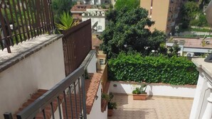 Eine Treppe führt zu einer Dachterrasse mit Metallgeländer, Pflanzkübeln und Blick auf die umliegenden Gebäude.