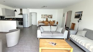 Un salon moderne avec un canapé gris, une table basse en bois et un coin repas comprenant une table et des chaises.