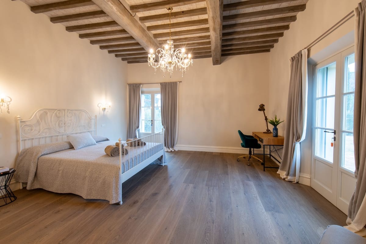 Ein Schlafzimmer mit Bett, Schreibtisch, Stuhl, einer Kandelaber und einem Fenster.