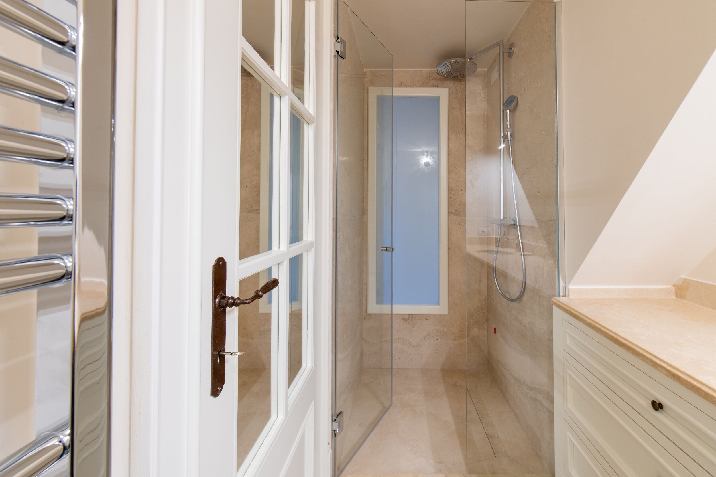 A bathroom with a glass shower enclosure, a white vanity, and a door with a brass handle.