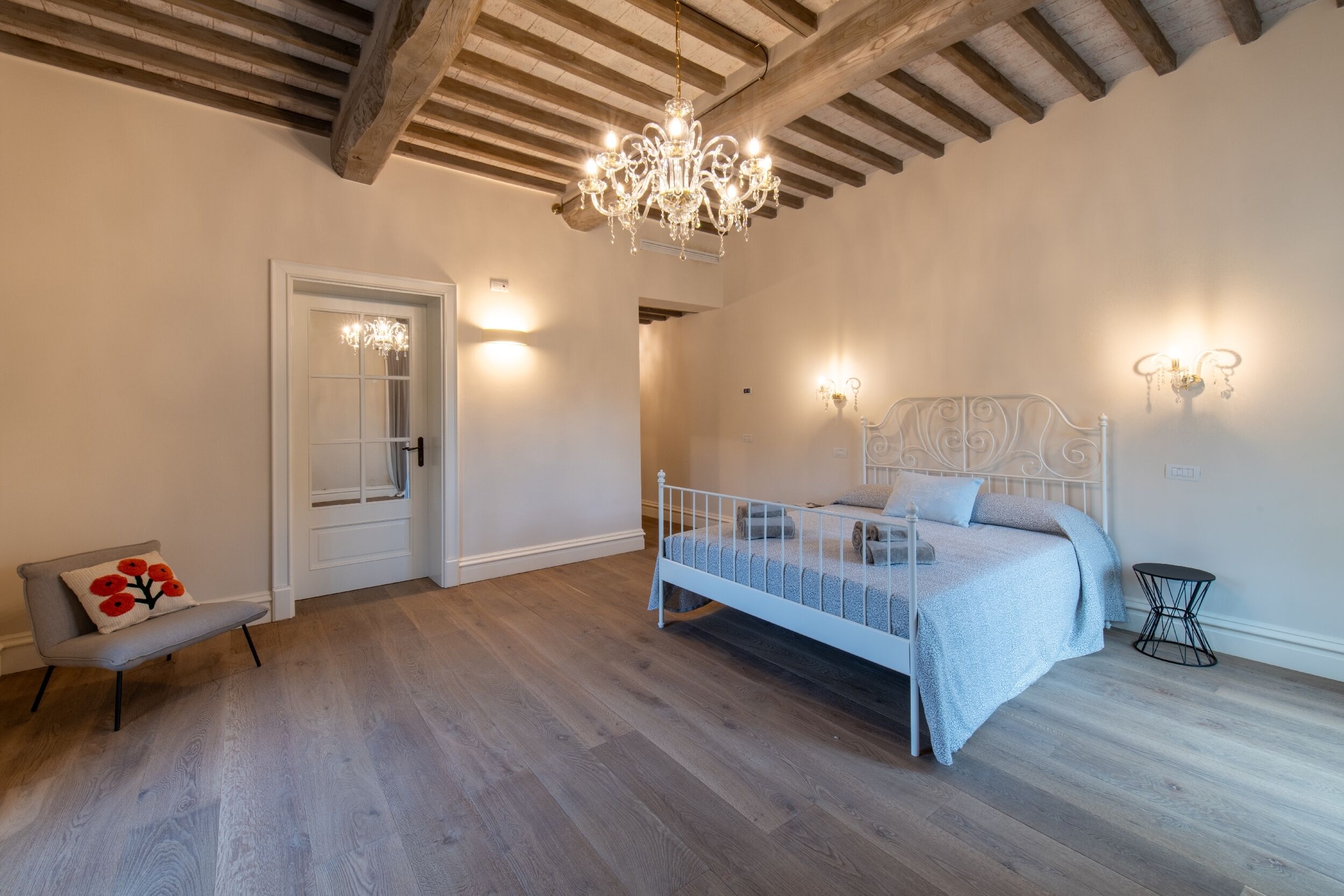 A bedroom with a bed, a bench, a chandelier, and wall sconces.