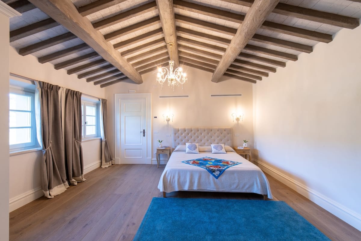 Ein Schlafzimmer mit Holzboden, einem großen Bett mit Patchworkdecke, Nachttischlampen und einer Kandelaberleuchte.